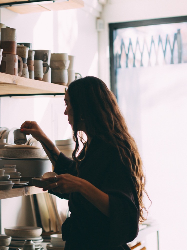 An artisan reaches for a piece on the shelves of a.r.c.'s pottery studio.