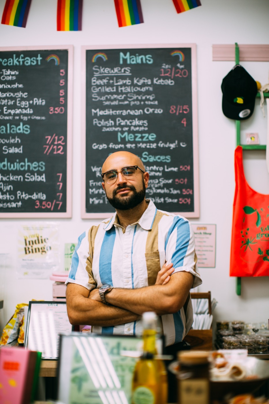 A café owner with arms crossed in front of his hand-lettered menu boards