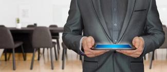 A man in a black suit in an office holding a tablet.
